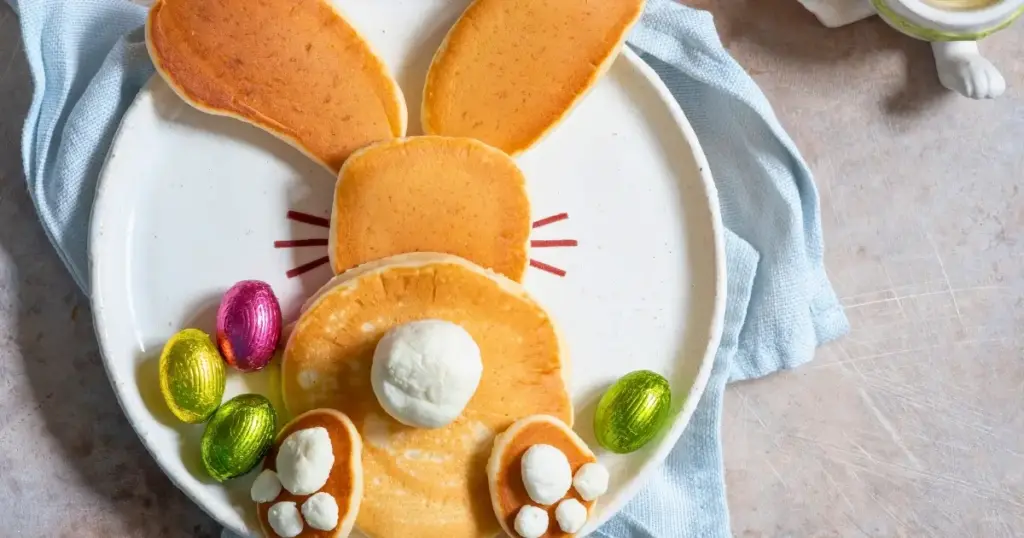 Pfannkuchen in Form eines Osterhasen von hinten, dekoriert mit Ostereiern, serviert zum Osterfrühstück für Kinder.
