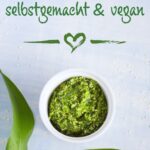 Helles, frisches Bärlauchpesto in einer weißen Schale auf blauem Hintergrund, umgeben von frischen Bärlauchblättern. Ideal für ein veganes Pesto-Rezept im Frühling – einfach selbstgemacht und vielseitig verwendbar.