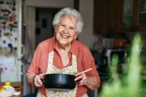 Lächelnde Oma mit Kochtopf in der Küche – Symbolbild für Omas Rezepte, traditionelle Hausmannskost und Rezepte wie früher